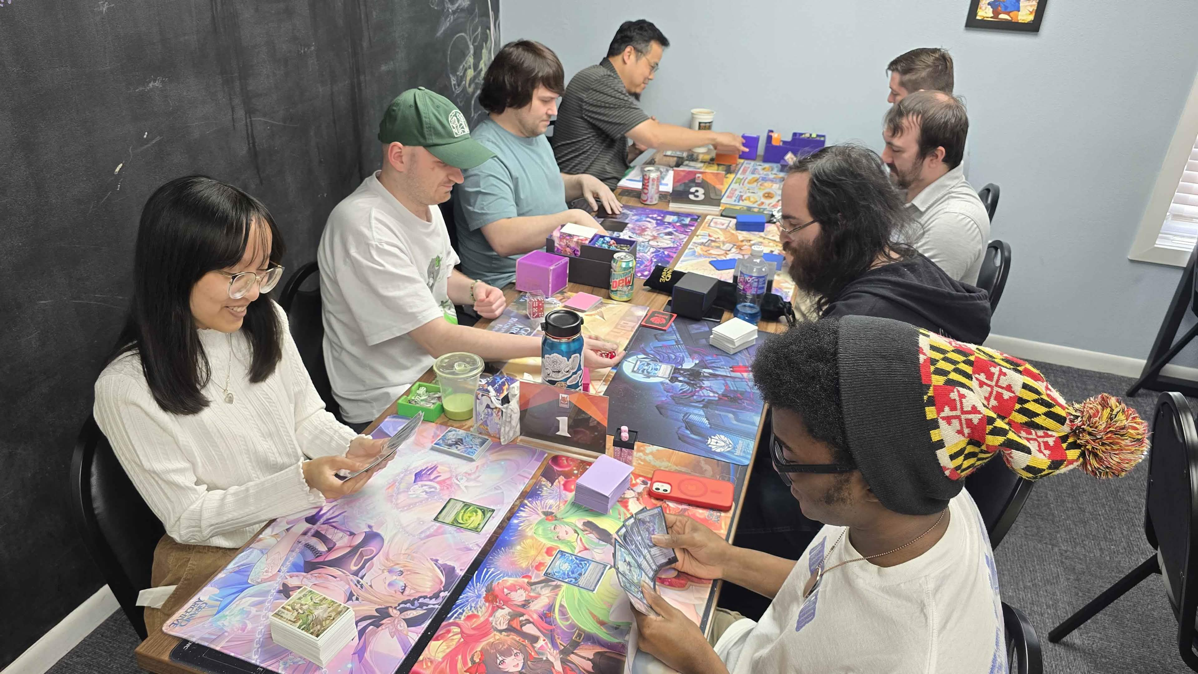 A table of players at a Grand Archive TCG event, playmats and card decks spread out during a match